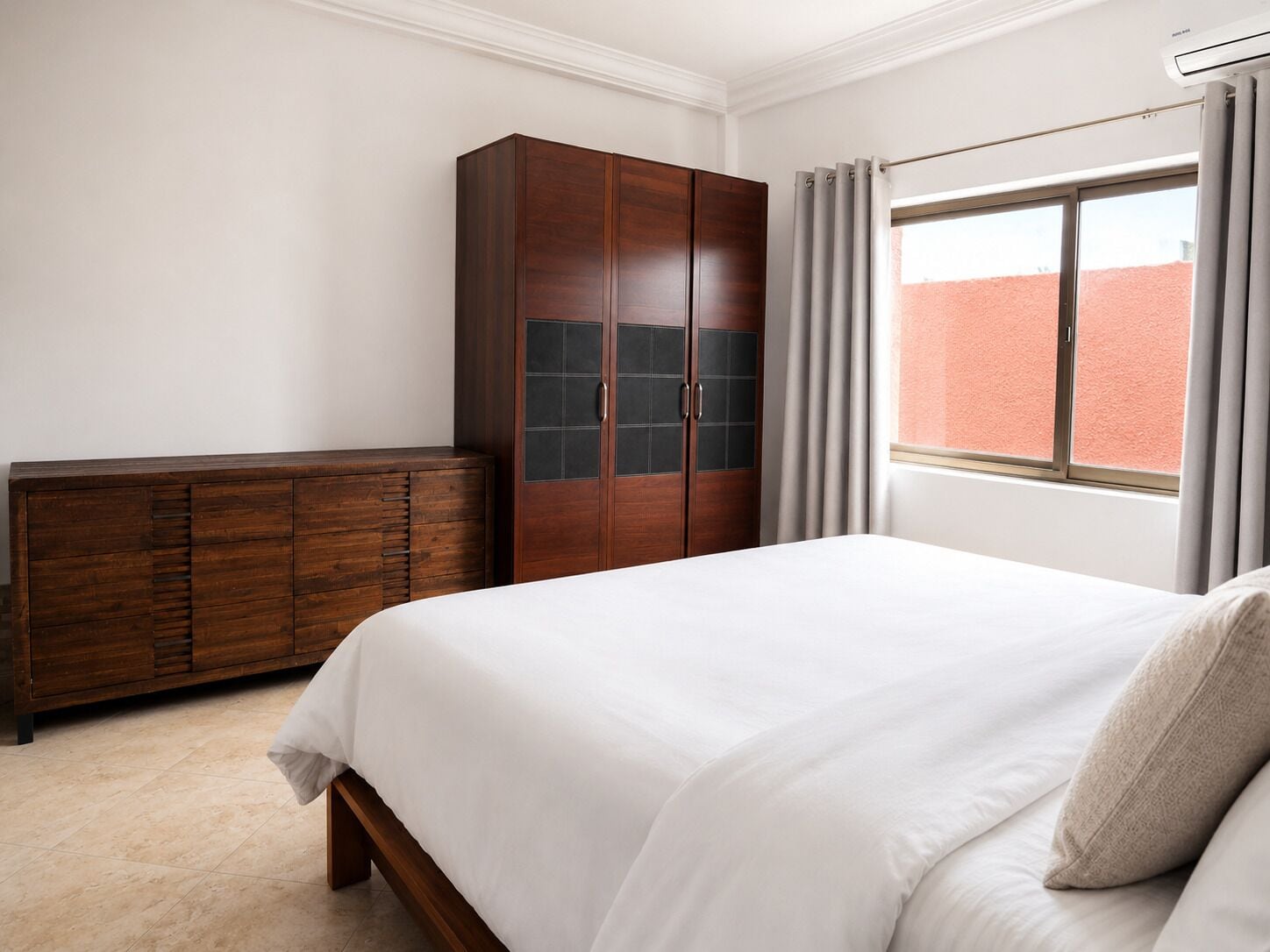 A bedroom with a bed, a wardrobe, and a window with curtains.