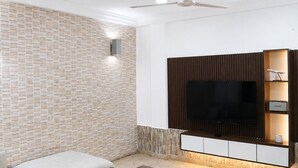 A modern living room with a flat-screen TV, a ceiling fan, and a built-in entertainment unit. - Luxor Garden Residence (Accra)