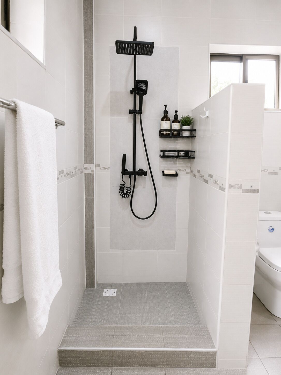 Ein modernes Duschbad mit einer in Glas eingefassten Dusche, einem Handtuchhalter und einer kleinen Ablage für Toilettenartikel.