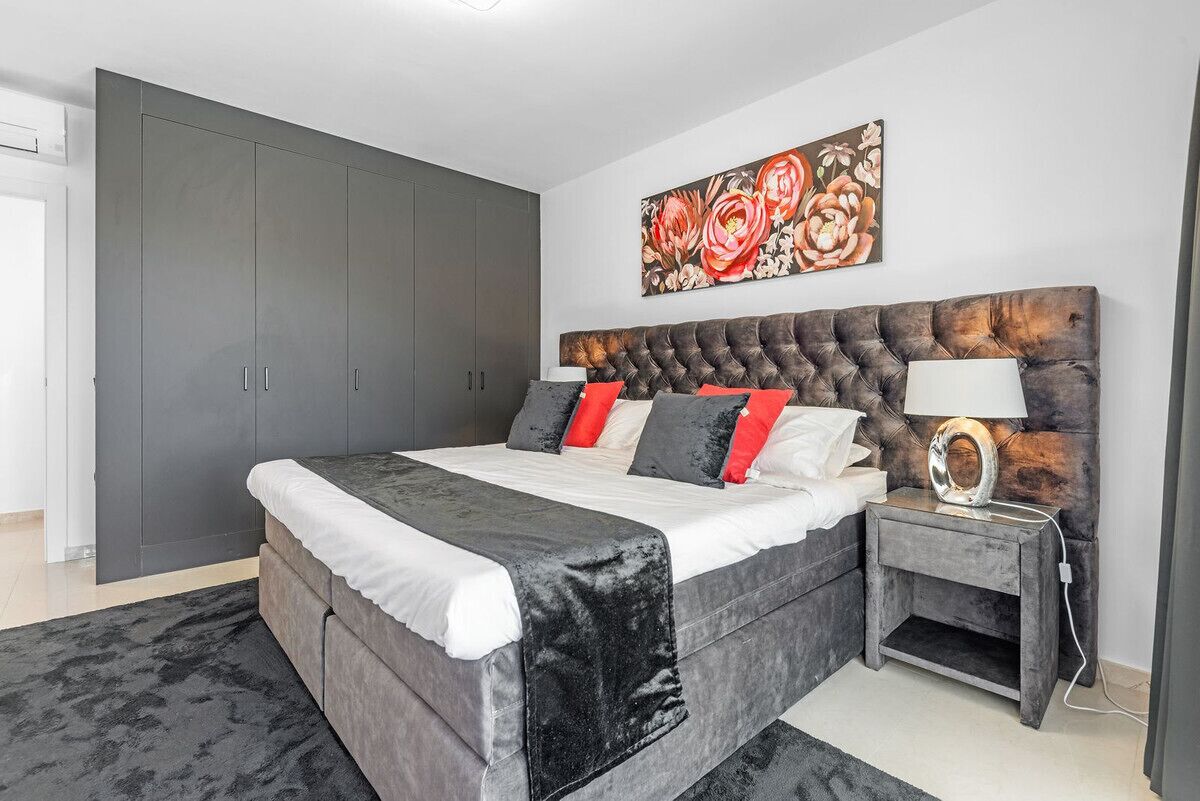 A bedroom with a large bed, grey wardrobe, and a painting on the wall.