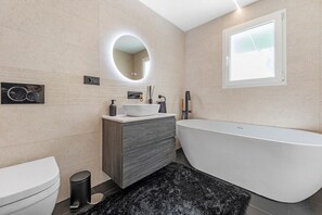 Un baño moderno con una bañera independiente, un tocador con espejo y un inodoro.
