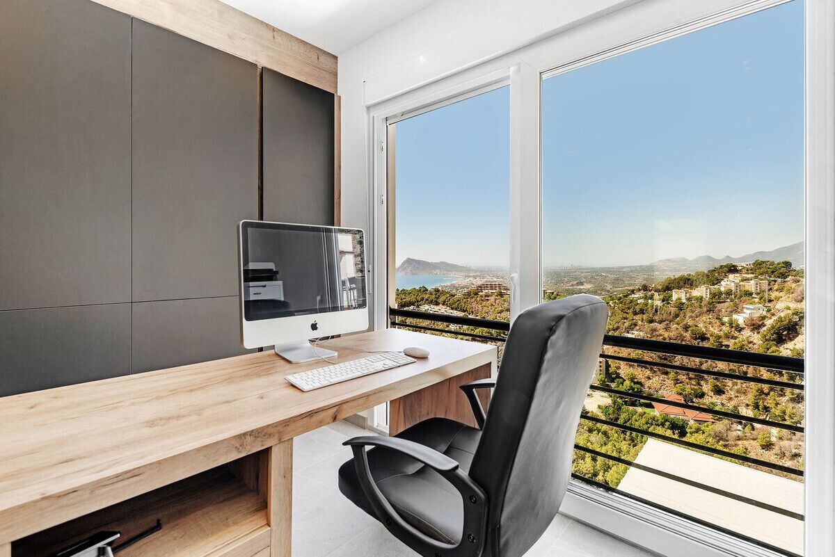 Un espace de bureau moderne doté d’une grande fenêtre, d’un bureau avec un ordinateur et d’une chaise.