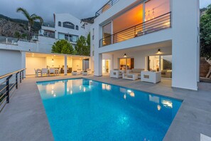 A modern two-story house with a swimming pool, outdoor seating, and a balcony.