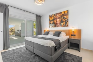 Un dormitorio con una cama grande, una puerta corrediza de vidrio a un balcón y una obra de arte colgada en la pared.
