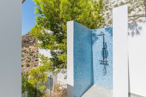 A pool with blue mosaic tiles, a shower area, and a view of a mountainous landscape.
