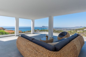 Un área de estar al aire libre con techo, mobiliario de mimbre y vista al mar.