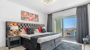 A bedroom with a large bed, a nightstand, a lamp, a painting, and a view of the outdoors. - Villa Azita is a spectacular Luxury Villa in Altea Hills, Panoramic Sea Views (Altea)