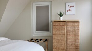 A bedroom with a bed, a window, an air conditioner, a wicker wardrobe, and a small potted plant. - Breeze Inn - Ibiza apartment, BioScience Park Leiden, beach, Leiden, (Oegstgeest)