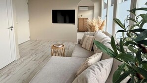 A modern living room with a sectional sofa, a small round table, and a large plant. - Breeze Inn - Ibiza apartment, BioScience Park Leiden, beach, Leiden, (Oegstgeest)