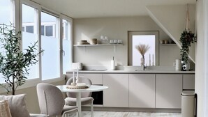 A modern living room with a sofa, a dining table, and chairs. There is a kitchen area with a refrigerator, a sink, and a countertop. - Breeze Inn - Ibiza apartment, BioScience Park Leiden, beach, Leiden, (Oegstgeest)