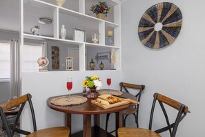 Ein Essbereich mit einem runden Holztisch, vier Holzsesseln, einer weißen Regalanlage mit Dekoration und einem runden Kunstwerk an der Wand.