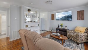 A living room with a beige sofa, patterned armchair, and a flat-screen TV mounted on the wall. - 2 Homes, Hot Tub,2 Kitchen, Nintendo, Big Parking (Lincolnton)