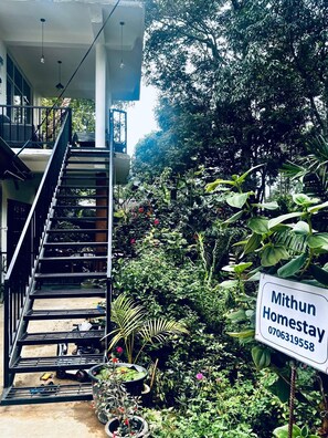 A staircase leading to a balcony with a lush garden and a sign for 'Mithun Homestay.' - Mithun Homestay (Ella)