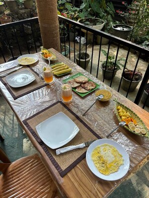 A dining table set with plates, glasses, and food items, surrounded by potted plants and a railing. - Mithun Homestay (Ella)