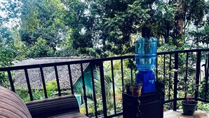 Ein Balkon mit schwarzem Metallgeländer, einem blauen Wasserspender und Topfpflanzen.
