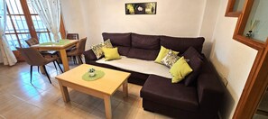 A living room with a brown sofa, yellow cushions, a wooden coffee table, and a dining area with chairs and a table.