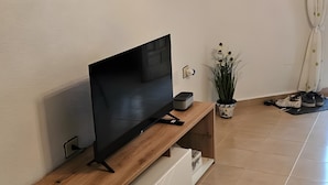 A living room with a flat-screen TV on a wooden TV stand, a potted plant, and a wall-mounted power outlet. - Holiday Home 'Marolesja' with Mountain View, Wi-Fi and Air Conditioning (Puerto de Mazarrón)