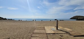 Een strand met een houten vogelzangpad dat naar het water leidt, een bewakingspost en rotsachtige richels.
