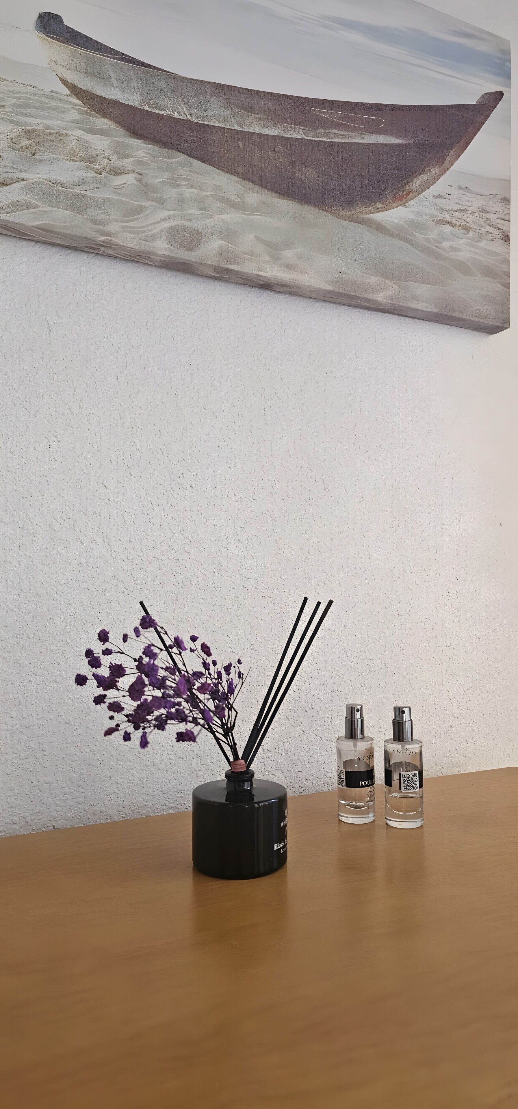 Ett träbord med en svart vas som innehåller lila blommor och två parfymflaskor.