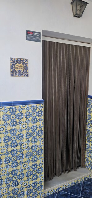 Une entrée d’immeuble avec un panneau indiquant la présence d’un service de sécurité, une plaque décorative et un rideau à rayures.