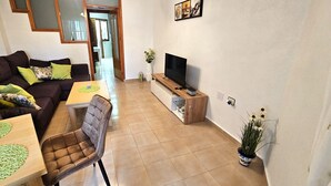 A living room with a sofa, a dining table, a TV, and a potted plant. - Holiday Home 'Marolesja' with Mountain View, Wi-Fi and Air Conditioning (Puerto de Mazarrón)