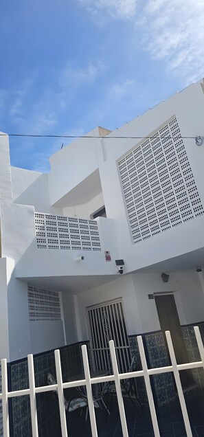 Een wit gebouw met een balkon, een hek en een beveiligingscamera.