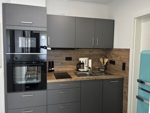 Ett modernt kök med gråa skåp, en inbyggd ugn, en kaffebryggare och en diskho.