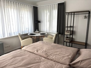 Ein Hotelzimmer mit Bett, einem kleinen Tisch mit Stühlen, einem Heizkörper und einem Regal mit Aufbewahrungsboxen.