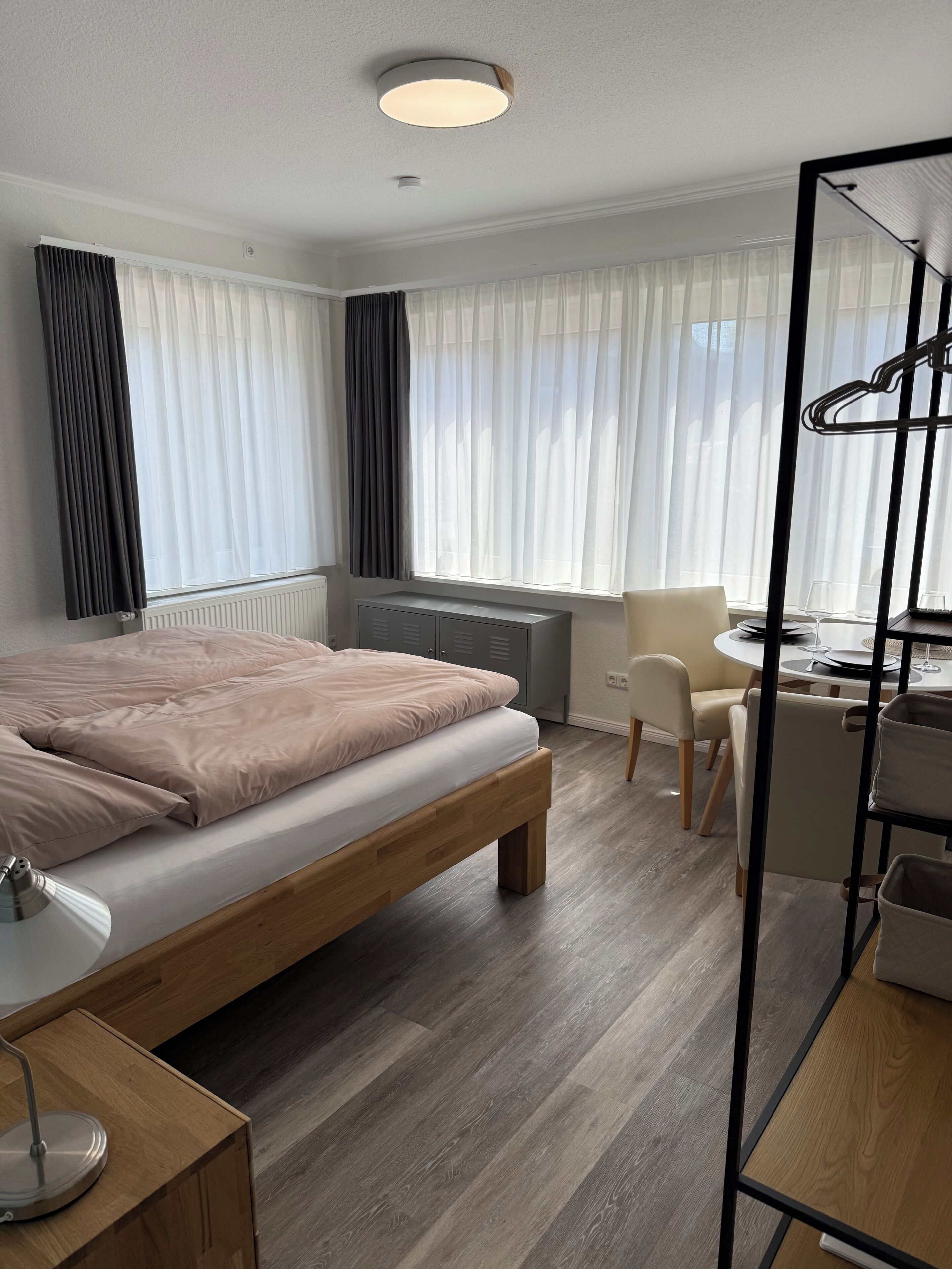 A modern hotel room with a wooden bed, a desk, a chair, and a dining table.. Newly furnished modern vacation studio in Wöhrden near Büsum