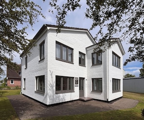 Une maison blanche à deux étages, construite en briques, avec de grandes fenêtres et une porte bien visible.