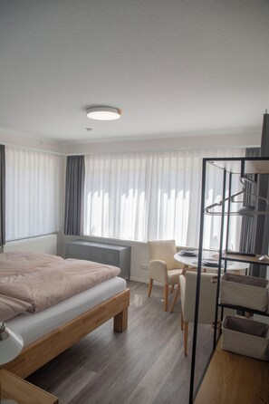 Una camera d'hotel moderna con un letto, una scrivania, una sedia, un termosifone e una finestra con tende.