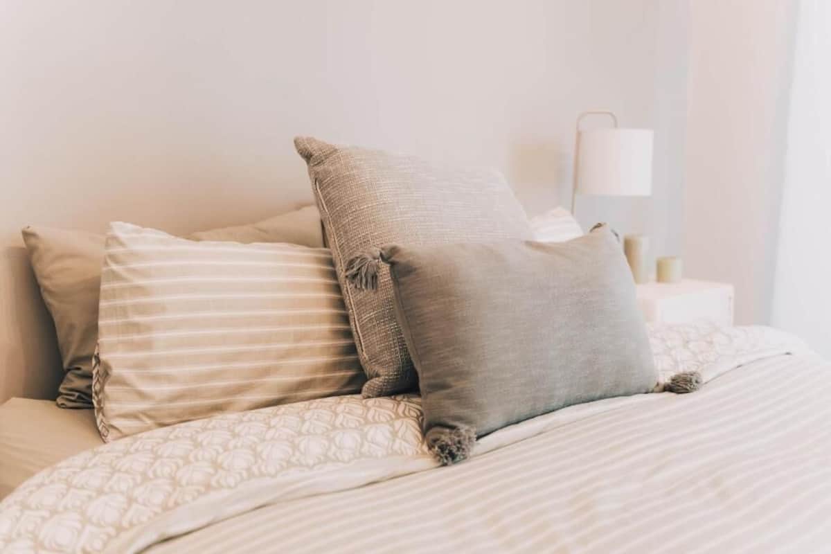 Una cama bien hecha con ropa de cama a rayas y varios almohadones.