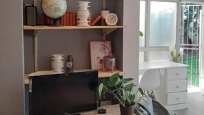 Un salon moderne avec un meuble TV en bois, des étagères ornées d’objets décoratifs, un fauteuil poire et une grande fenêtre.
