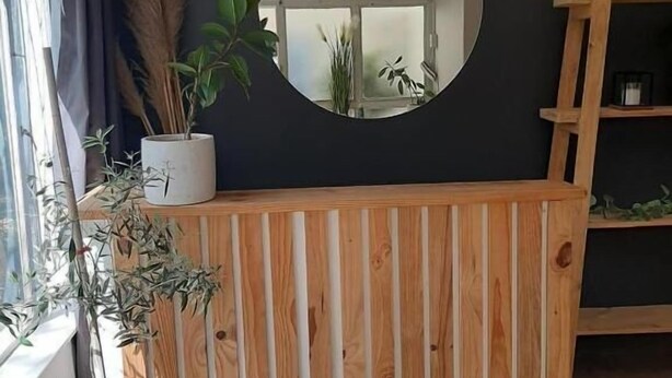 Un comptoir d’accueil en bois, un miroir rond, un luminaire suspendu en osier et une plante en pot.
