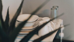 Une pile d’assiettes blanches et une tasse blanche sur une table, avec une plante au premier plan.