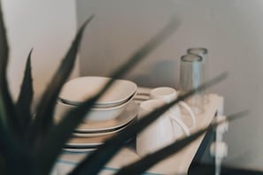 A stack of white plates and a white cup on a table, with a plant in the foreground. - Leaf & Lark (Bloemfontein)