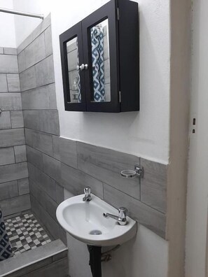 A bathroom with a white sink, a black cabinet with a mirror, and grey tiled walls. - Leaf & Lark (Bloemfontein)