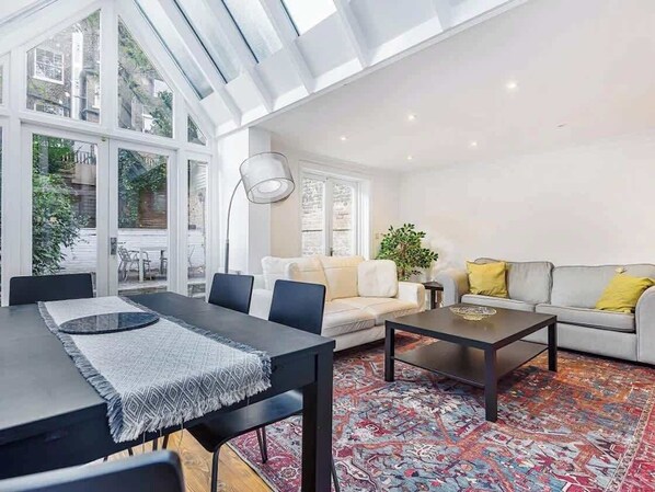 A spacious living area with a dining table, sofa, and coffee table, large windows, and a view of the outdoors. - Sunny, 2bed 2bath, garden apartment near Hyde Park (London)