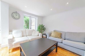 A modern living room with a white sofa, a grey sofa, a dark coffee table, and a wall clock. - Sunny, 2bed 2bath, garden apartment near Hyde Park (London)