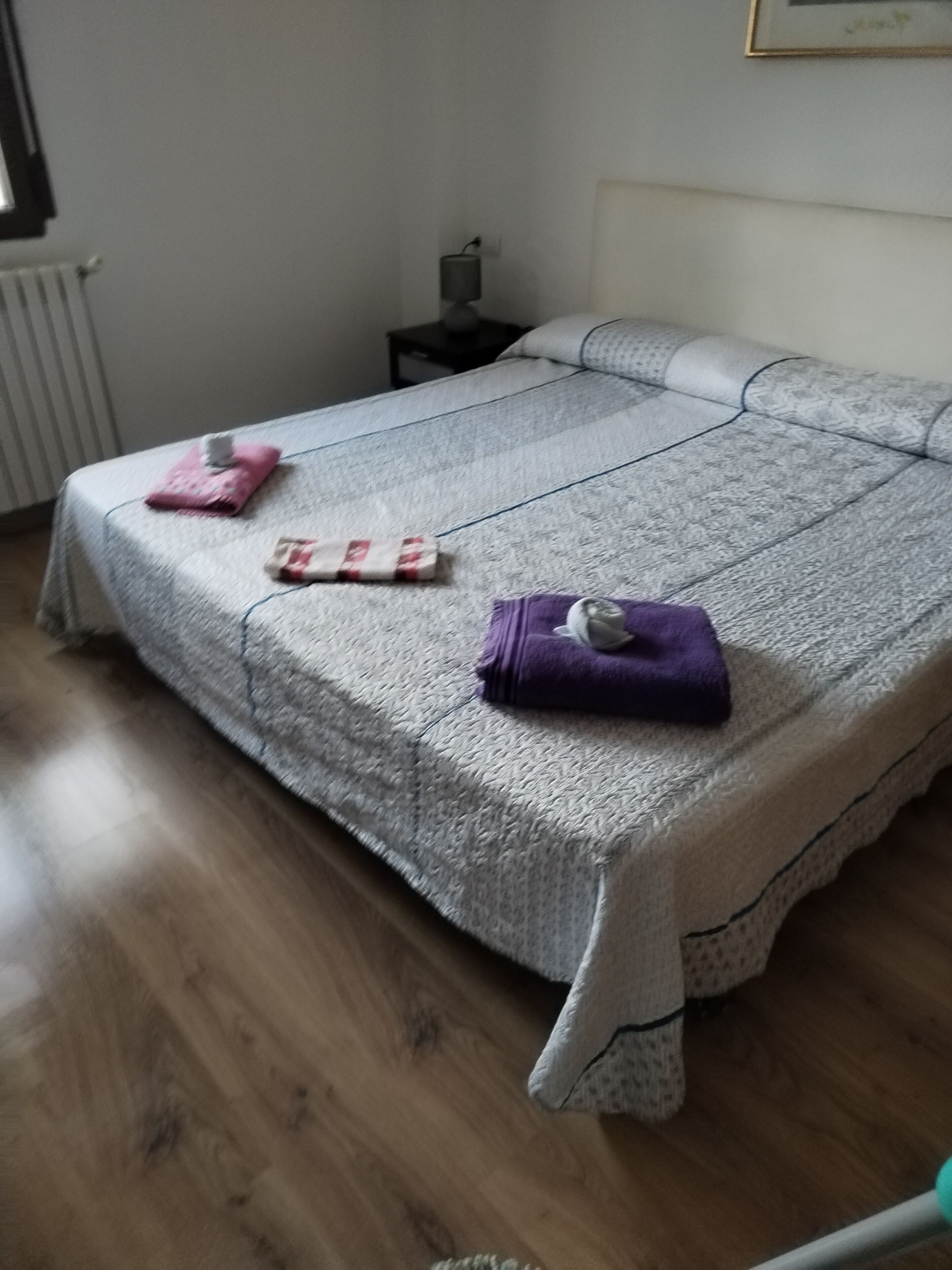 Ein ordentlich gemachtes Bett mit einer gemusterten Tagesdecke, einem Kopfkissen und zwei gefalteten Handtüchern.