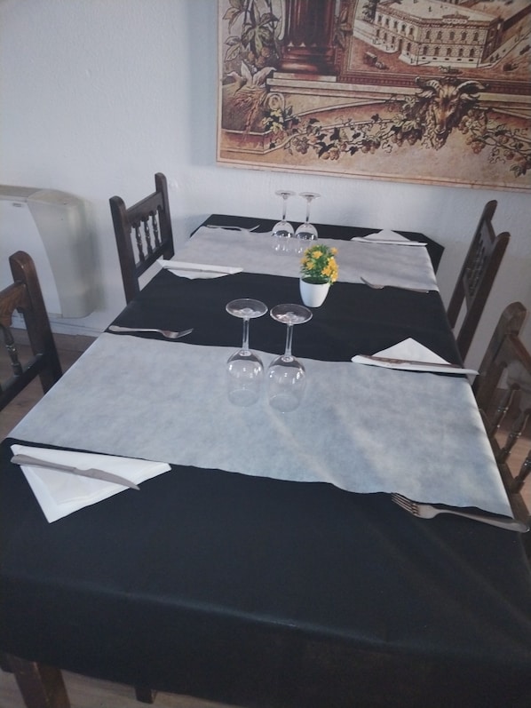 Ein Esstisch, gedeckt mit Weingläsern, einer Vase mit gelben Blumen und einer schwarzen Tischdecke.