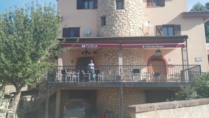 Un bâtiment doté d’une tour en pierre, d’un espace extérieur couvert aménagé en coin salon et d’une voiture garée devant.