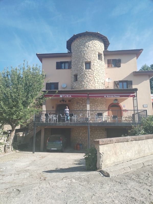 A building with a stone tower, a covered outdoor seating area, and a car parked in front.