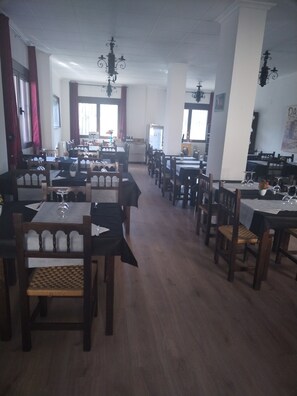 Un restaurante espacioso con varias mesas y sillas, una barra central y apliques decorativos en las paredes.