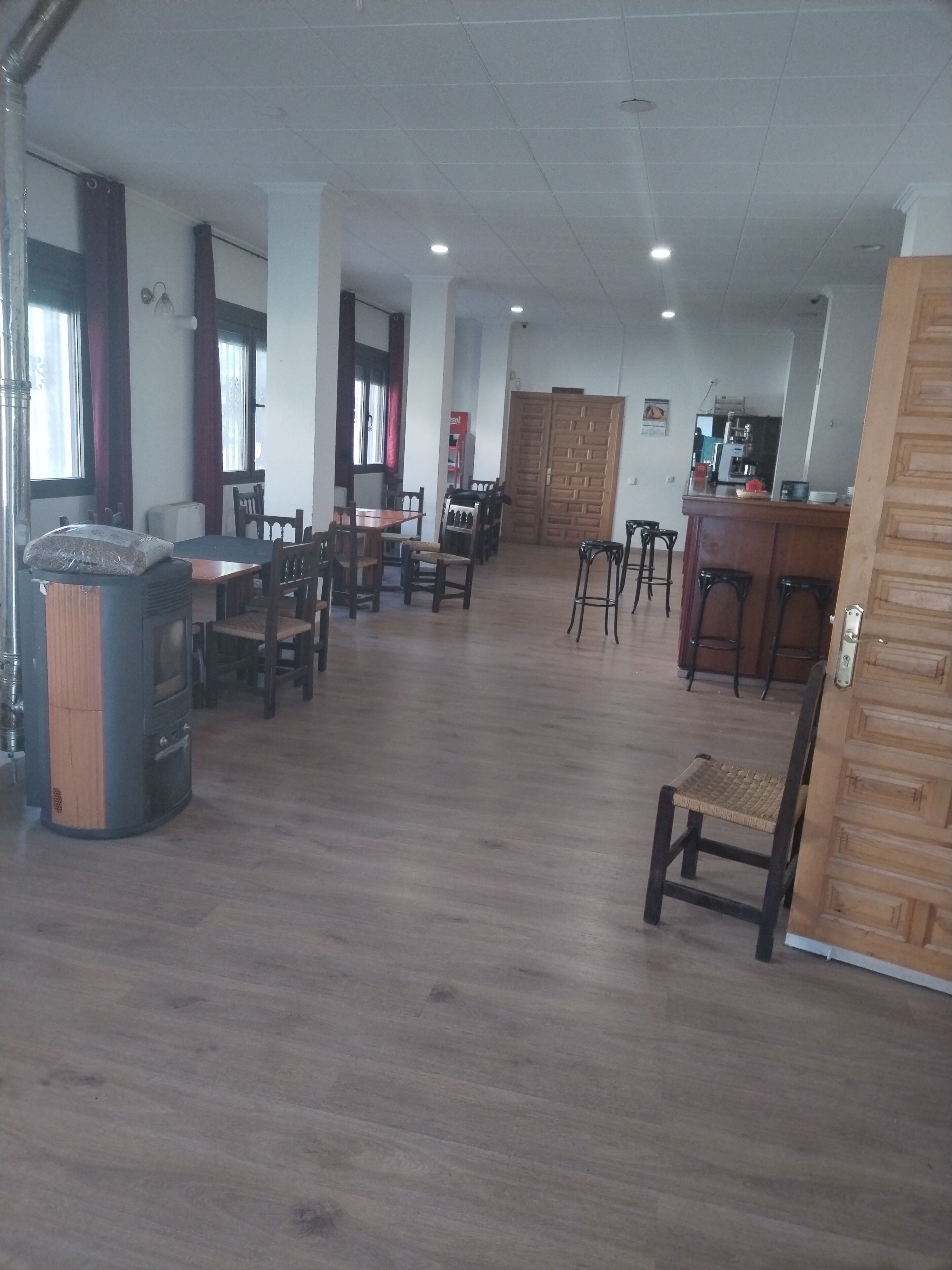 Un comedor amplio con varias mesas y sillas, una barra con taburetes y un armario de madera.