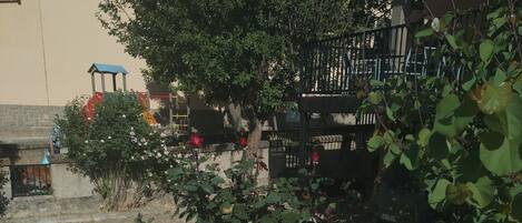 Un muro de piedra con una sombra, un árbol y un edificio con un letrero.