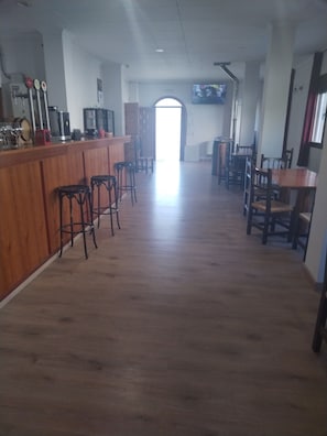 Eine Bar mit Barhocker, einer Holztresen und einem an der Wand befestigten Fernseher.