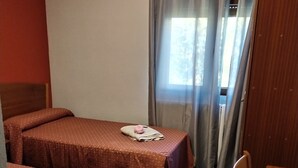 Una habitación con dos camas, una mesa de madera, una silla y una ventana con cortinas.