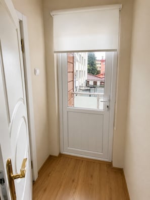 A narrow hallway with a wooden floor, a white door with a brass handle, and a window with a white blind. - Kadıoğlu otel (Bursa)