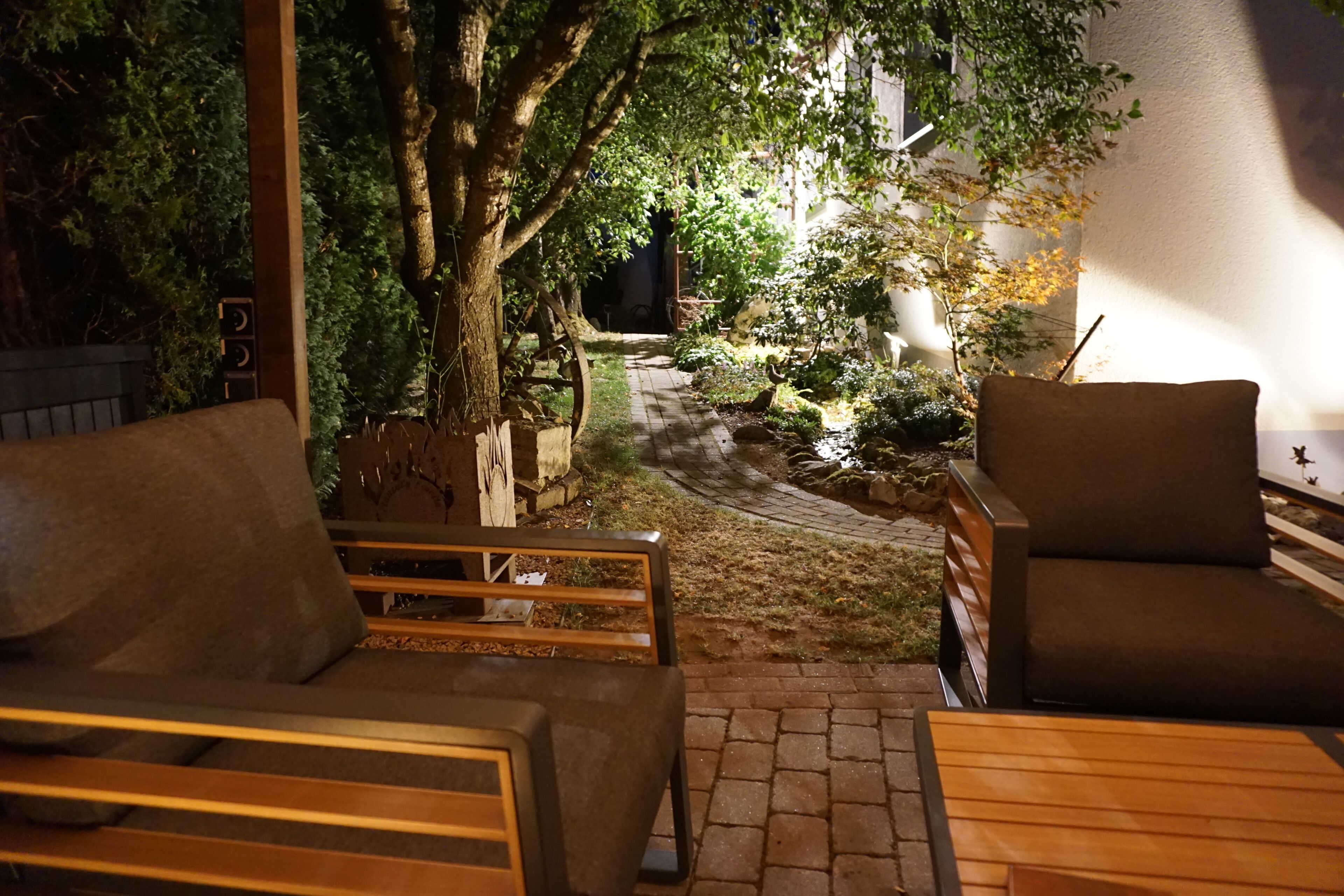 Un espacio al aire libre con mobiliario de madera, un sendero empedrado y un árbol.